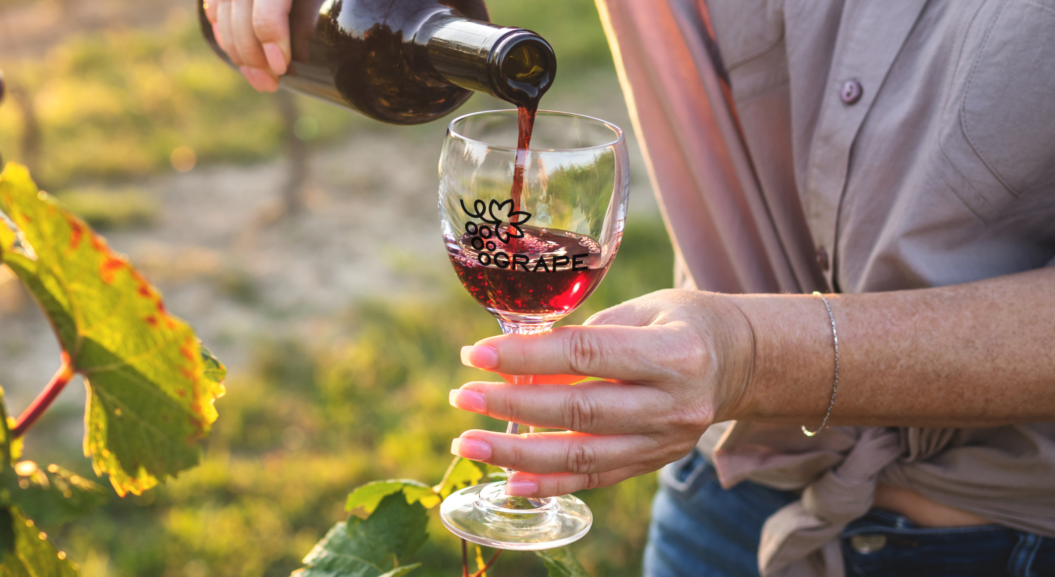 Person with vineyard in background, pouring wine into custom wine glass with logo